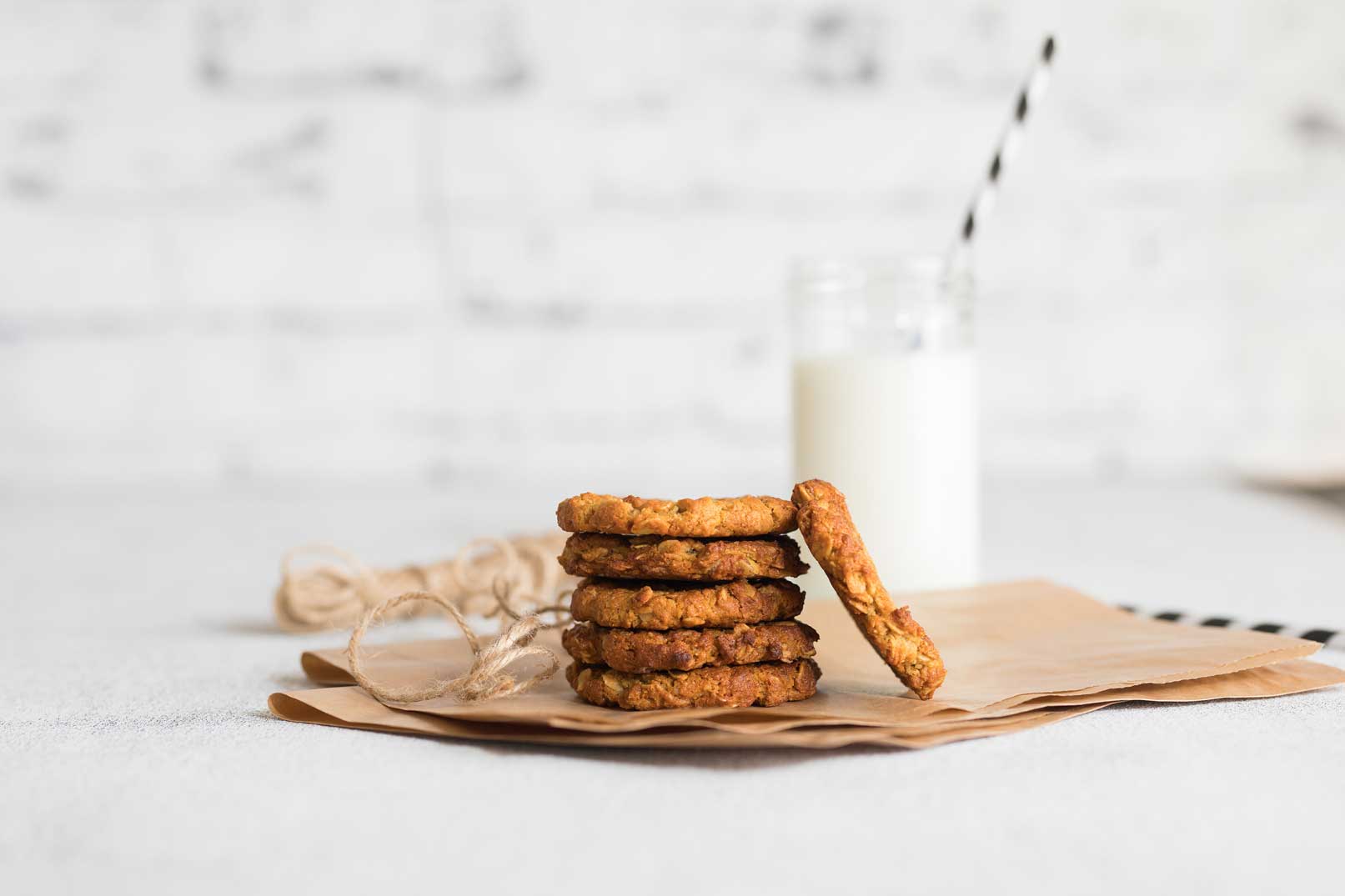 baked Anzac biscuits stacked on brown paper bag for packing served with a glass of milk