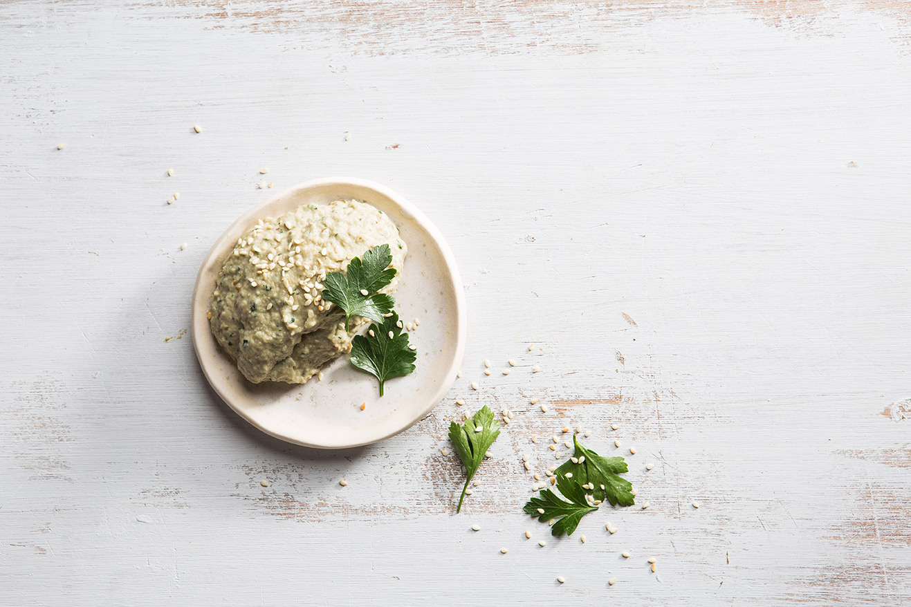 Image of a white dish with babaganoush and a sprinkle of coriander on the top and side shot from above