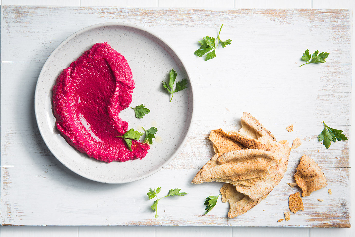 Image of roast beetroot hummus on a serving plate with baked pita on the side and herbs to garnish, shot from above