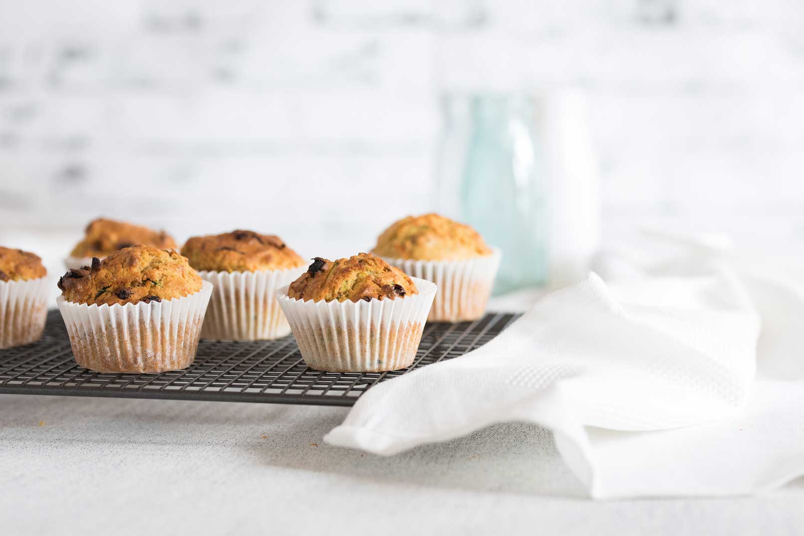 Baked carrot and zucchini muffins on a wire cooling rack with a white cloth napkin on and jug of water in the background.