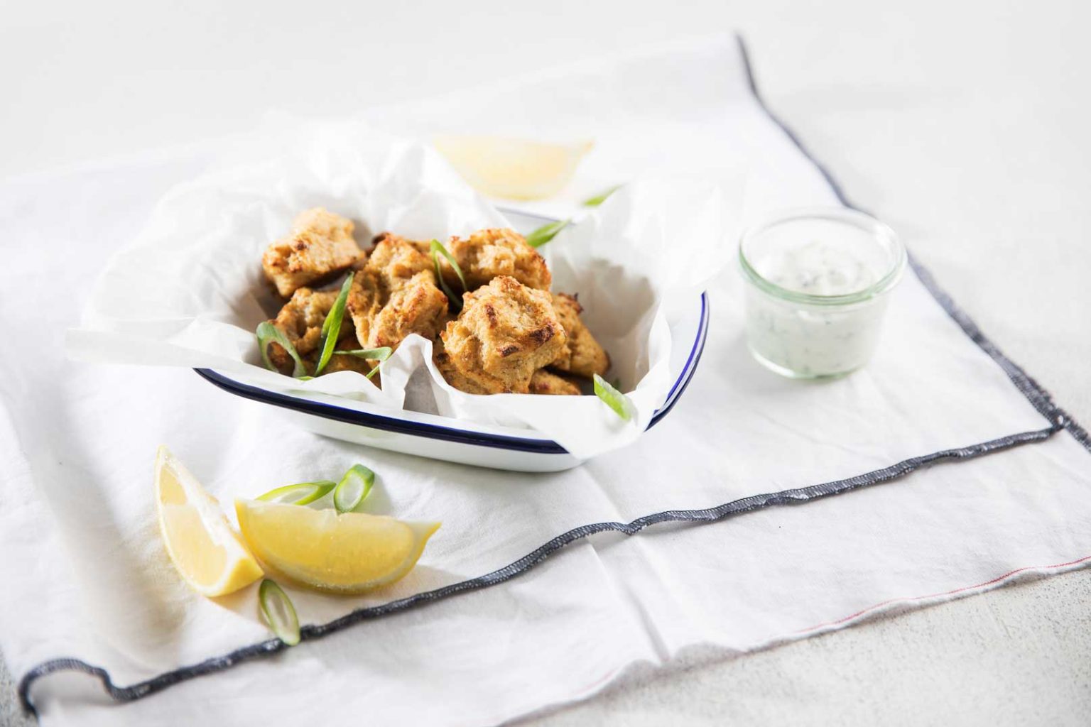 Cauliflower nuggets on baking paper in a small serving dish with dipping sauce and lemon wedges to serve.