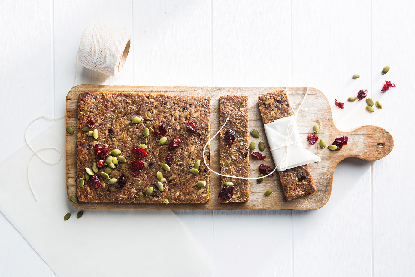Image of a block of baked chewy nut and seeds bars ready to be sliced on a wooden chopping board.