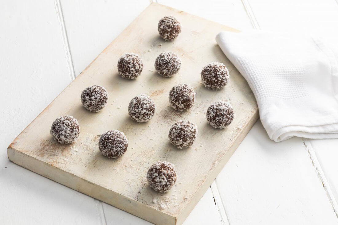 Chocolate, Honey & Coconut Bliss Balls on a timber board with a folded white napkin on the right
