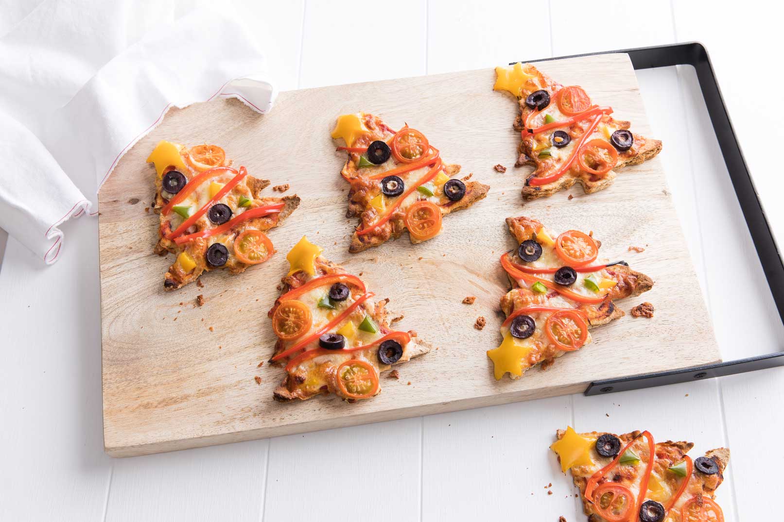 Alt: Seven baked Christmas tree pizzas served on a wooden chopping board.