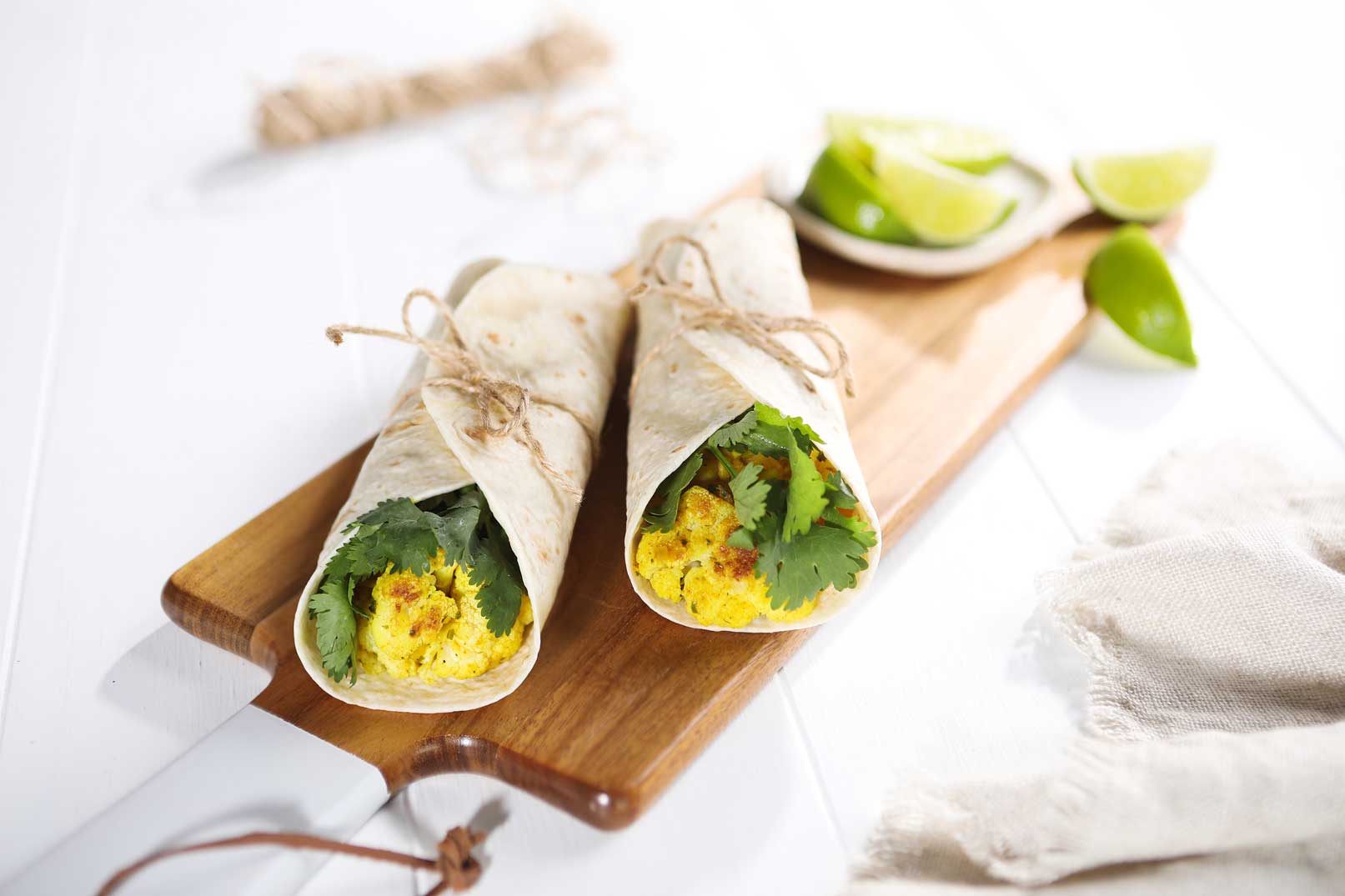 Two curried cauliflower and roti wraps on a chopping board with lime.