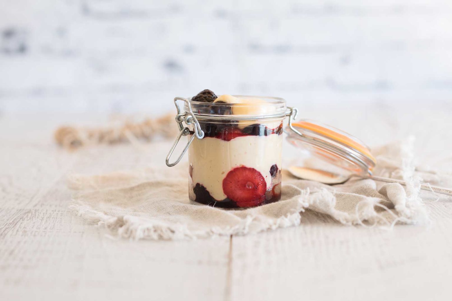 Custard pudding served in a glass jar with the lid open sitting on a rustic cloth napkin.