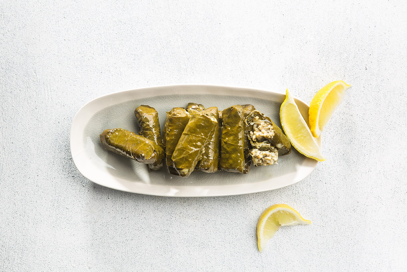 Image of dolmades arranged on a long serving dish with a side of lemon wedges to serve, shot from above