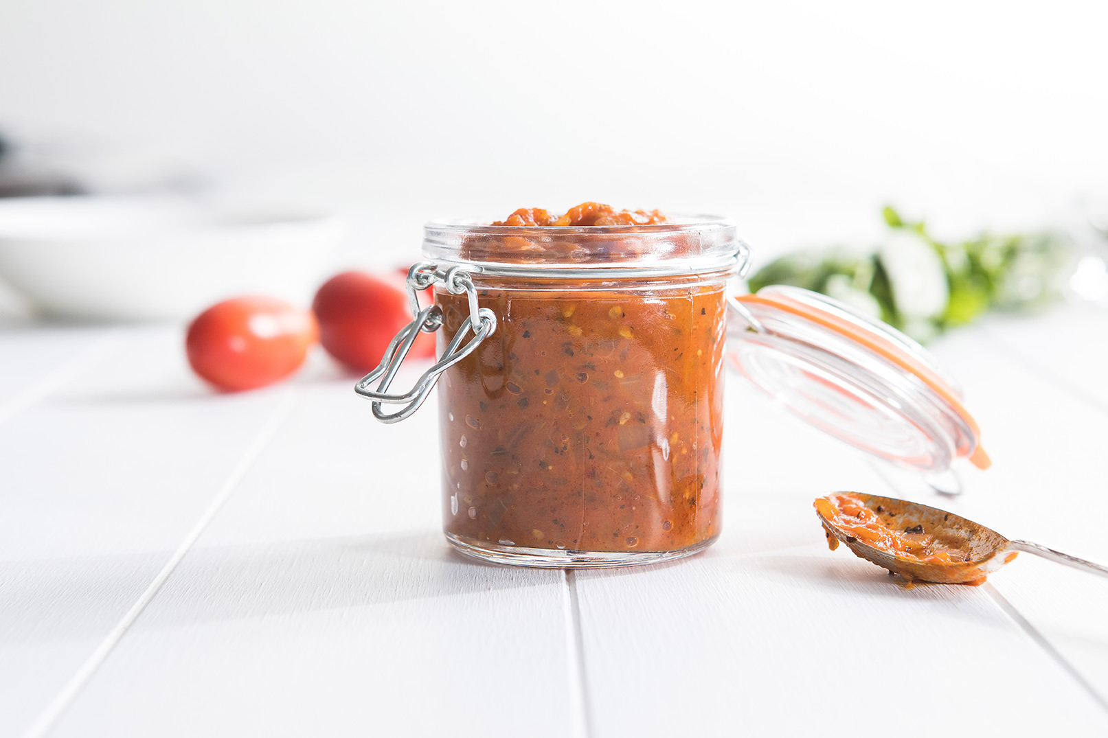 Image of fresh tomato sauce in a jar with tomatoes in the background and a serving spoon