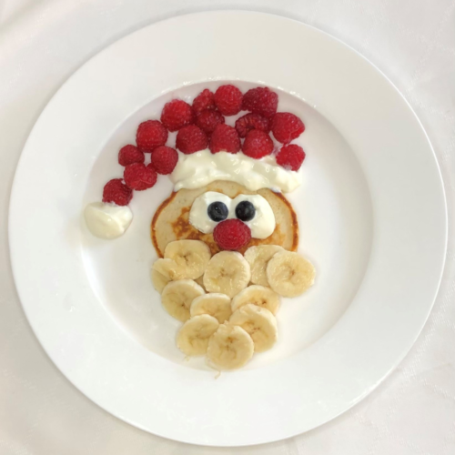 santa face made from pikelets , sliced bananas, scream and raspberries