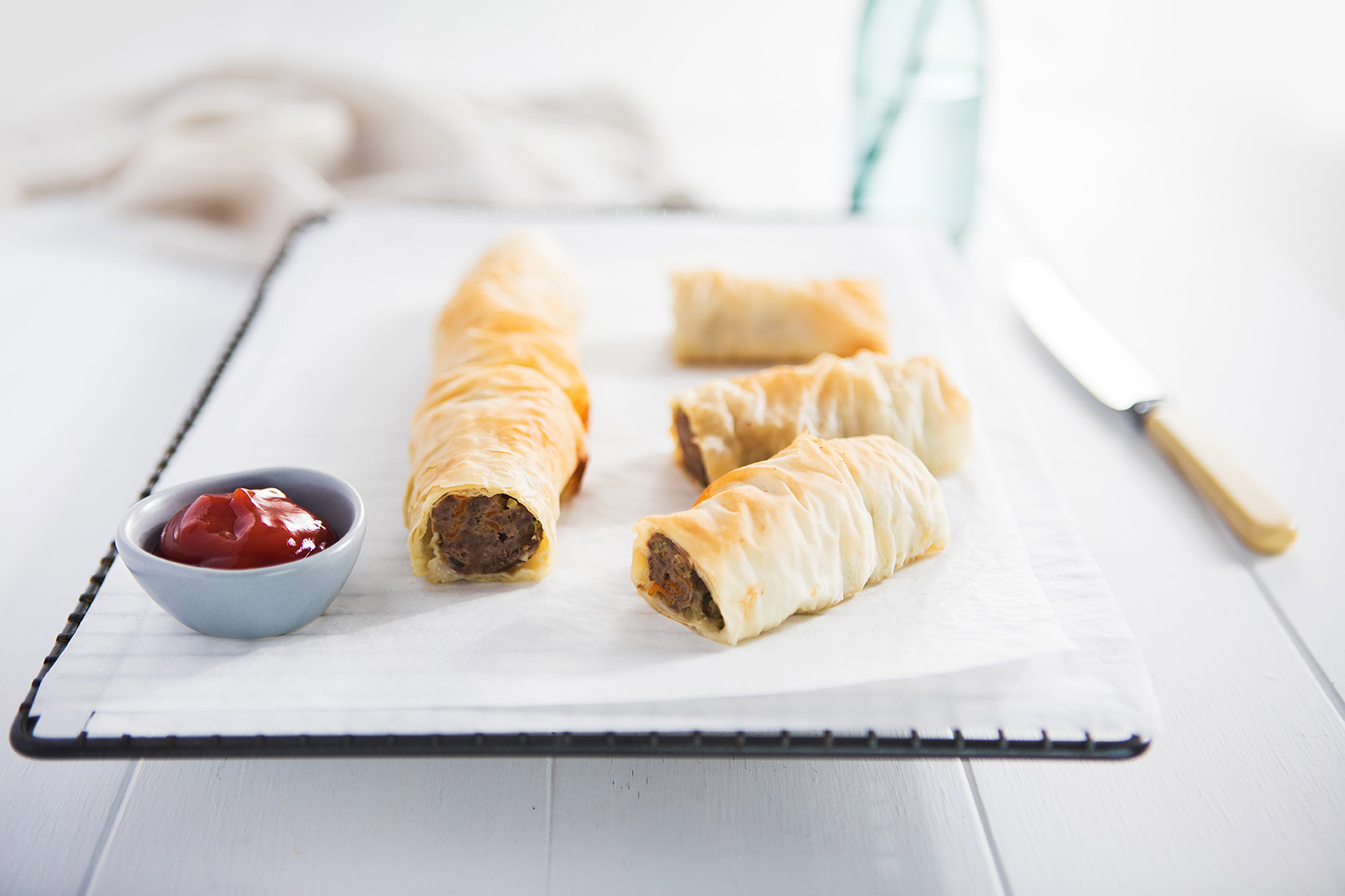 Image of five baked hidden veg sausage rolls on baking paper cooling on a baking tray with tomato sauce in a small bowl on the side