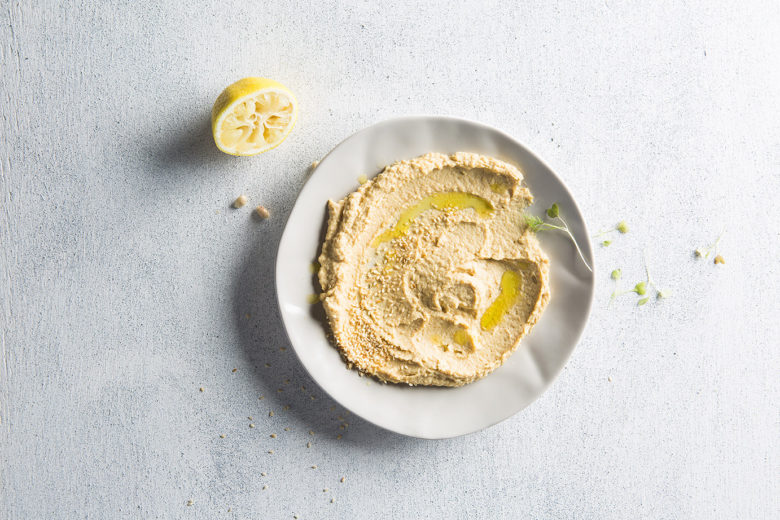 Image of a large platter of hummus with half a lemon on the side, shot from above