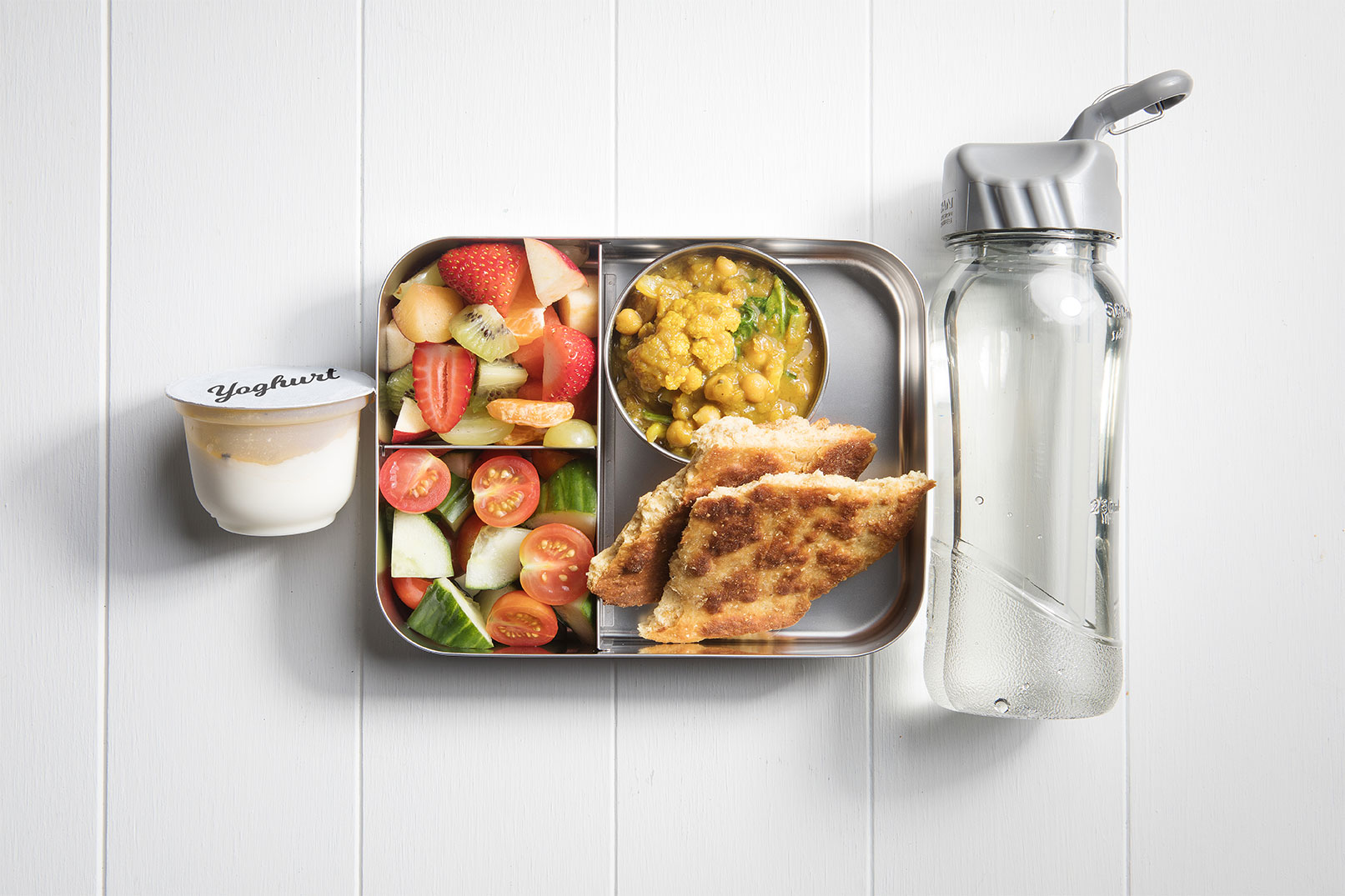 Image of a packed lunch box with cauliflower and spinach dahl, naan bread, csalad and a yoghurt tub and bottle of water on the side