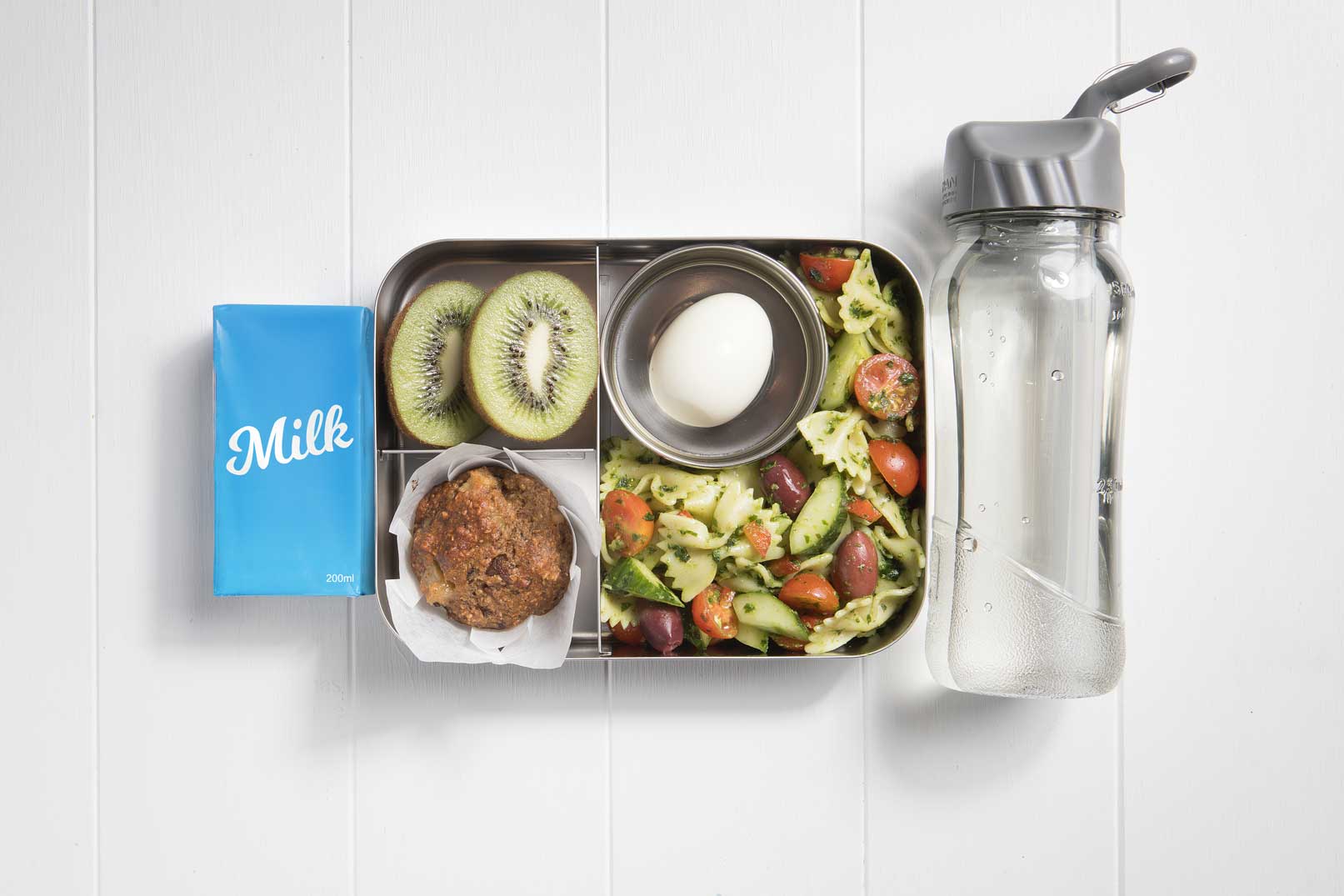 Top view of packed lunch box with salad, muffin, egg, kiwifruit, milk popper and a water bottle.