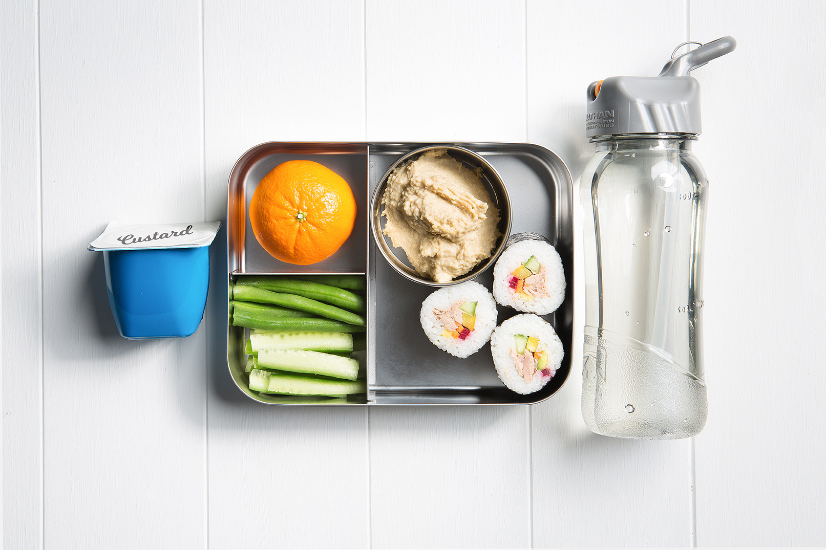 Image of a packed lunch box with rainbow sushi pieces, mandarin, green beans and cucumber, hummus and a custard tub and bottle of water on the side