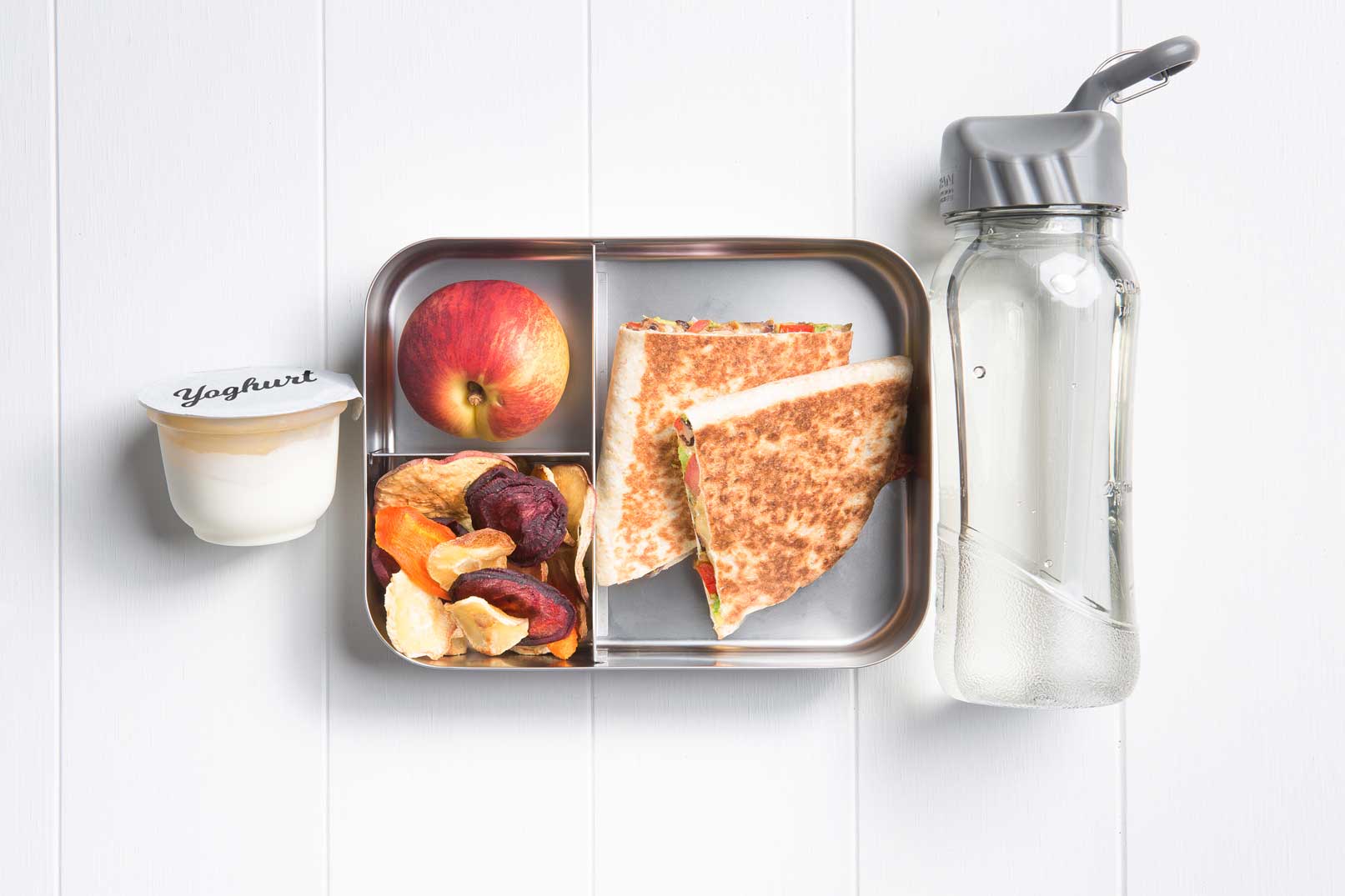 Image of a packed lunch box with two black bean quesadilla, nectarine, baked vegie chips and a yoghurt tub and bottle of water on the side