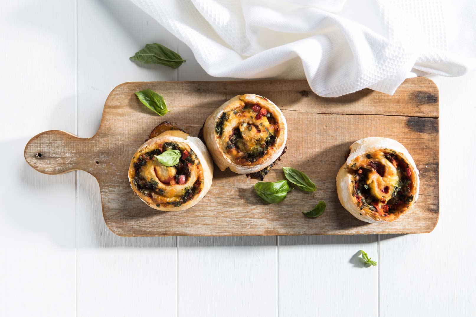 Image of three baked Mediterranean scrolls shot from above, sprinkled with basil leaves on a wooden serving board.