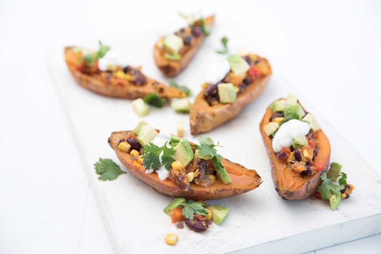 five Mexican baked sweet potatoes topped with reduced-fat yoghurt and coriander leaves served on a wooden serving board.