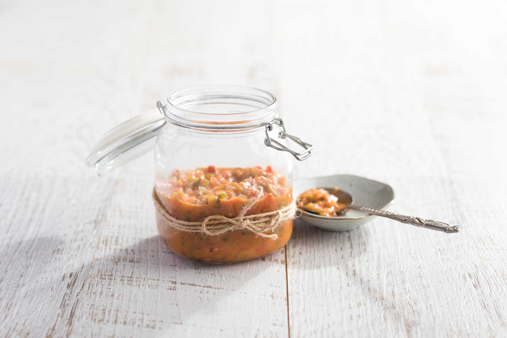 Mexican salsa in a glass jar wrapped with a twine bow with a serving spoon on the side.