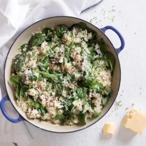 Mushroom risotto bake in a large round oven proof dish with blue handles shot from above and a chunk of parmesan cheese and white cloth napkin on the side.