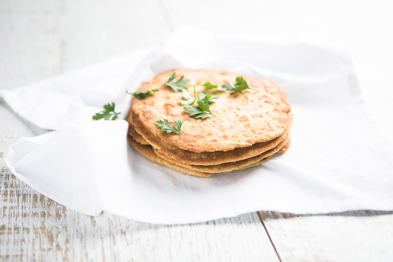 Image of three pieces of naan bread stacked in a pile on a plain cloth napkin and sprinkled with parsley