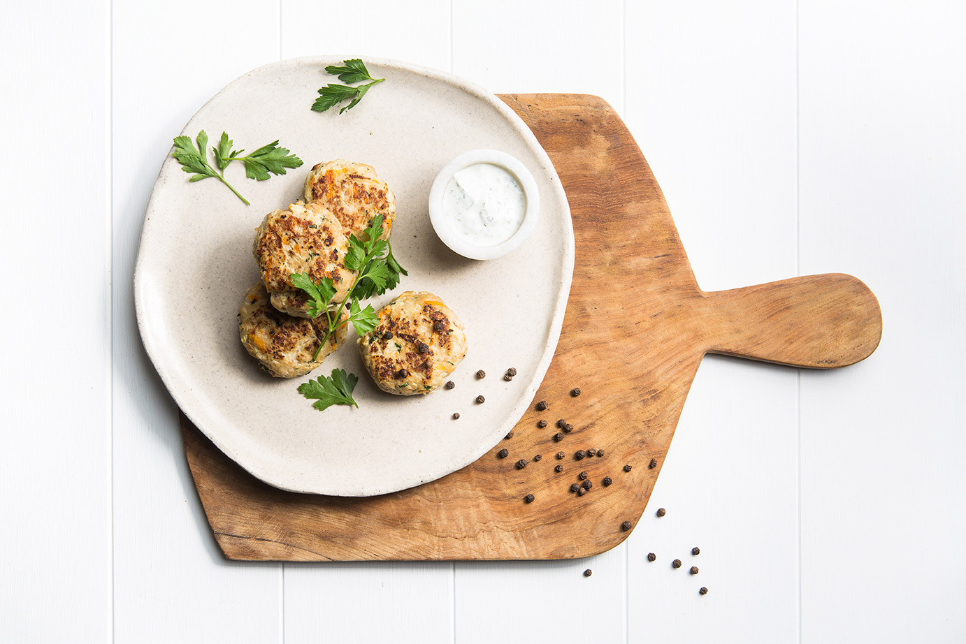 Image of four pork and apple Rissoles on a large stone plate served on a wooden cutting board with parsley, cracked paper and a small dish of dipping sauce on the side
