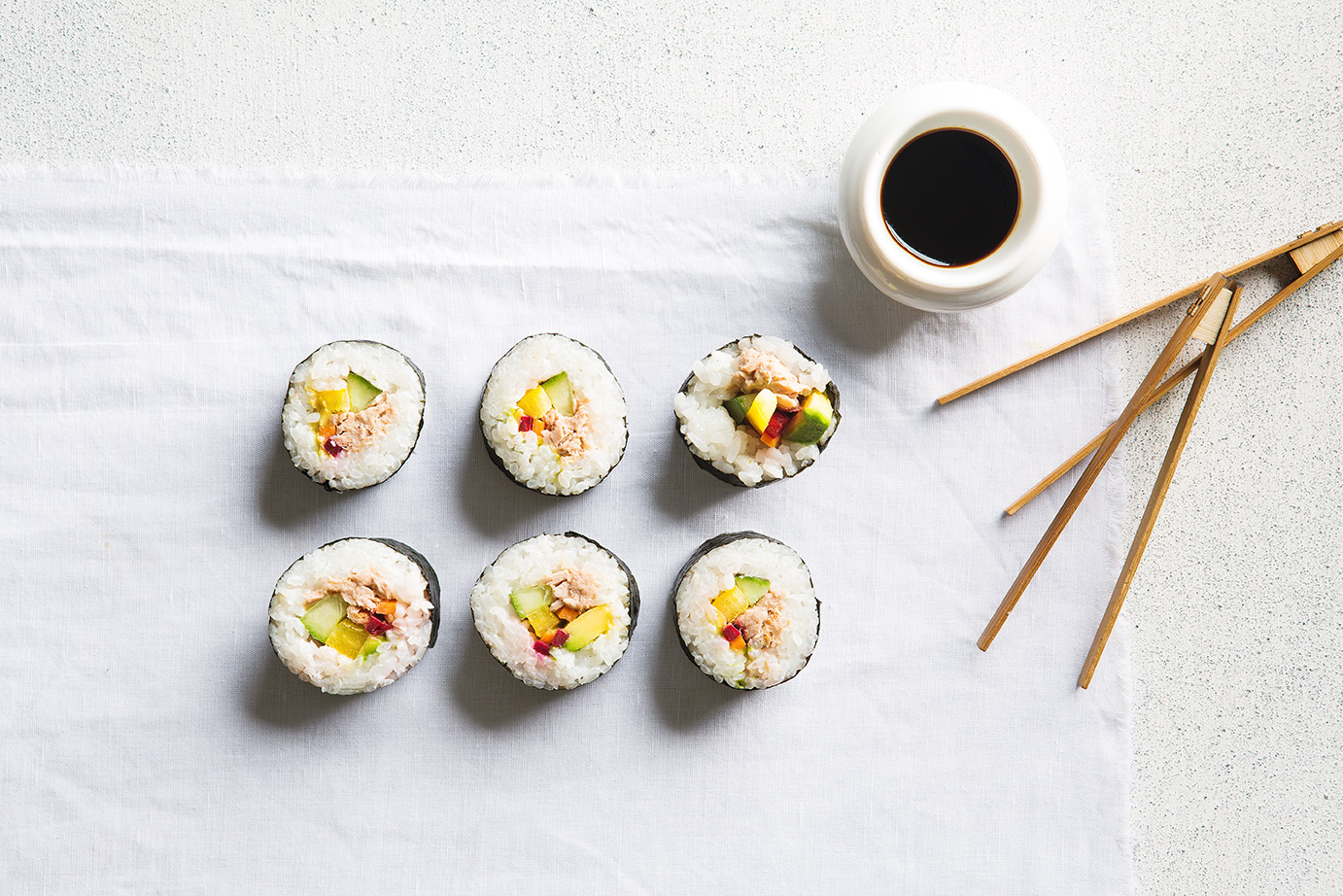 Image of six pieces of rainbow sushi served on a cloth napkin with dipping sauce and wooden chopsticks on the side
