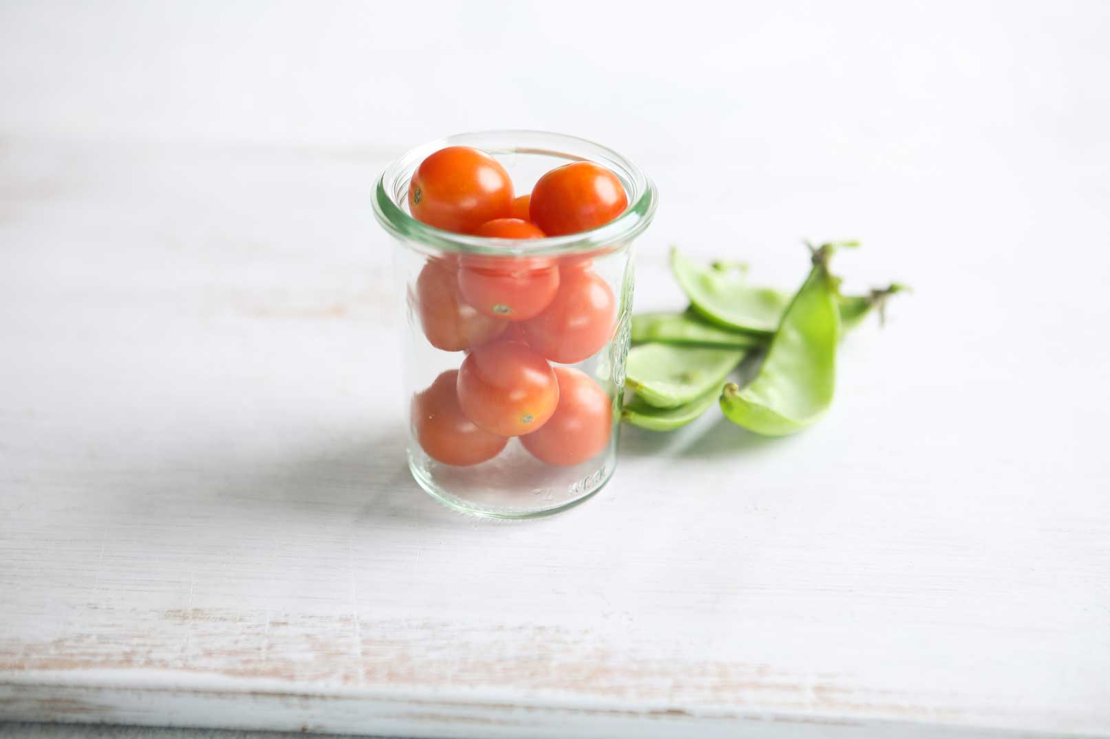 Cherry tomatoes in a glass jar with a handful of snow peas on the side