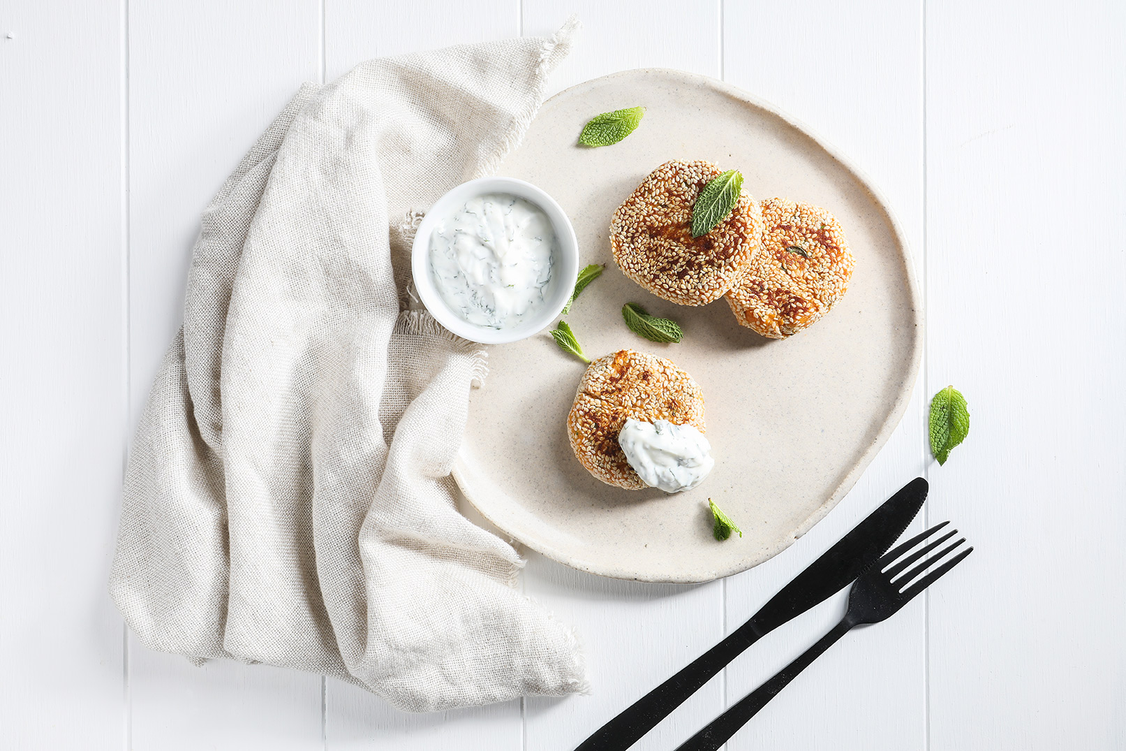 Image of three sweet potato falafels on a large plate with minty yoghurt dip and a knife and fork