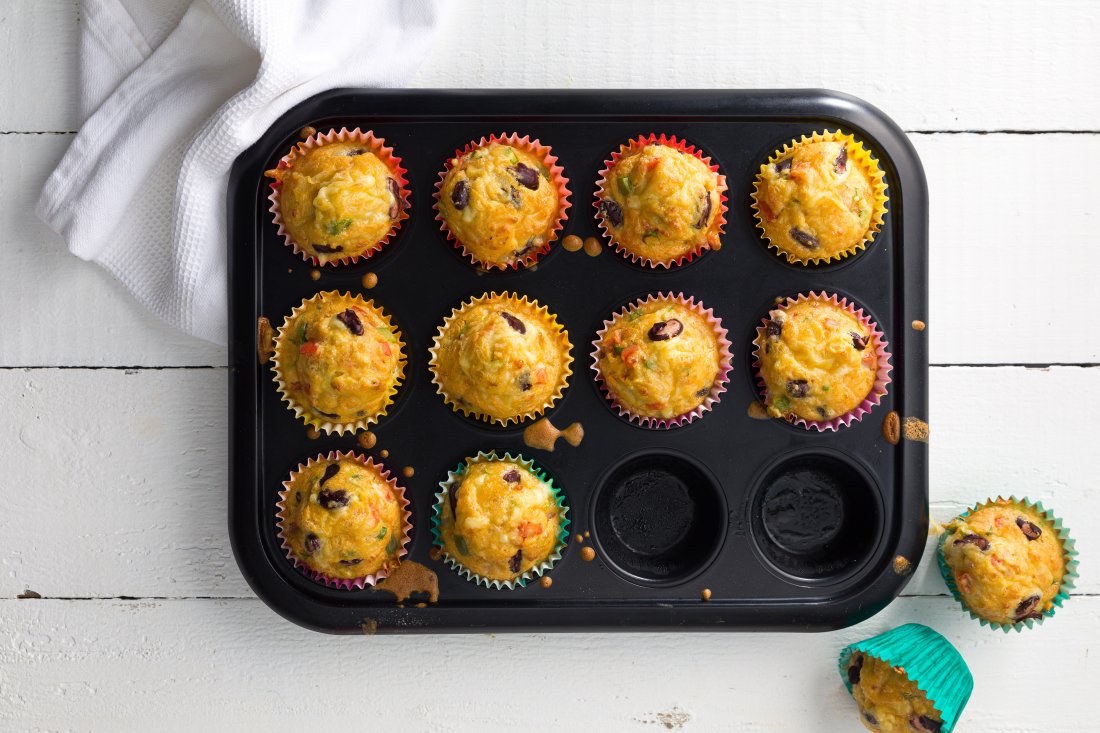 10 muffins in a black muffin tin with 2 muffins removed and sitting on the right side with a white napkin top left.