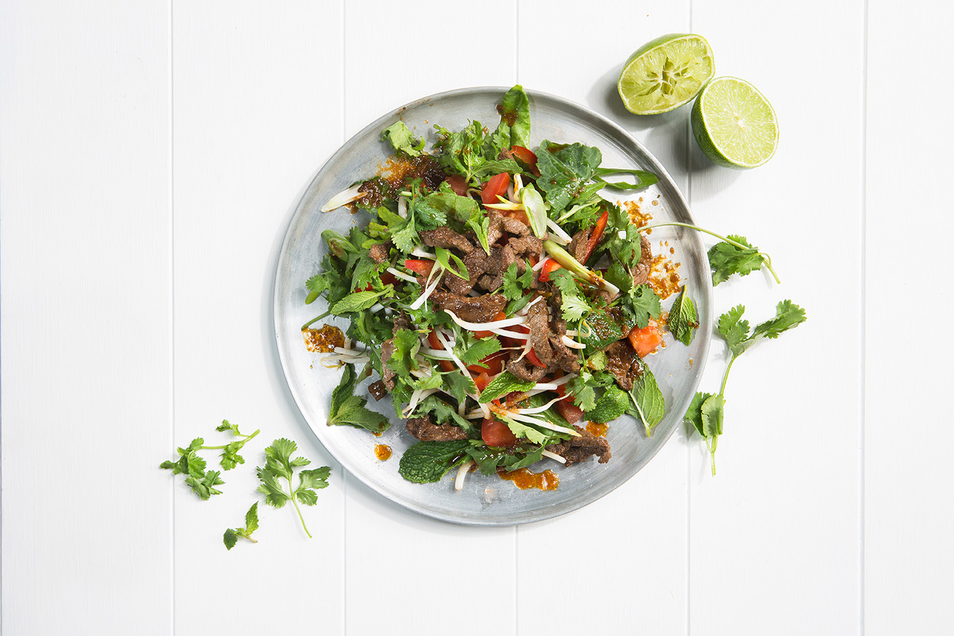 Image of thai beef salad on a silver serving plate with two lime wedges to serve.