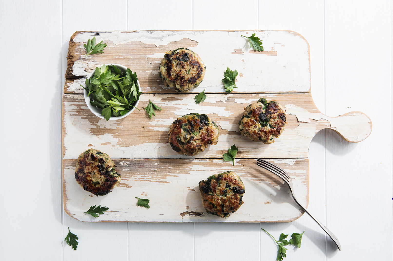 Image of five Turkey and Spinach Rissoles served on a large wooden cutting board with a fork and herbs on the side