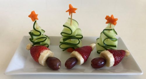 Three Christmas trees made from cucumbers and carrot star, three Santa hats made form strawberries, banana and grapes