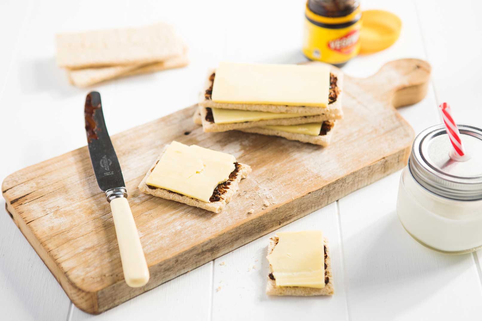 Crispbreads spread with vegemite and cheese on a wooden chopping board and a container of milk