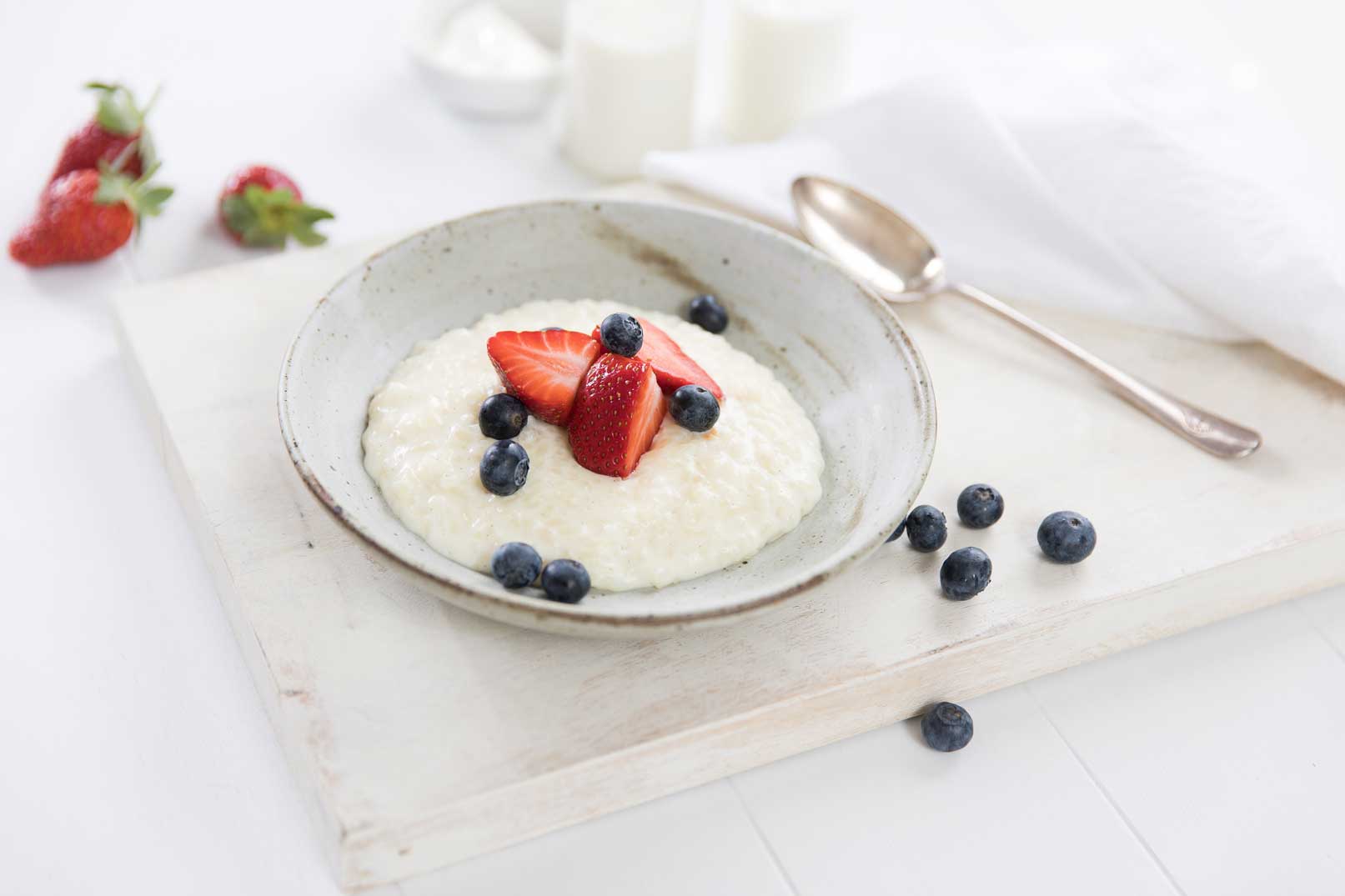 Yoghurt rice pudding topped with sliced strawberries and blueberries in a white bowl