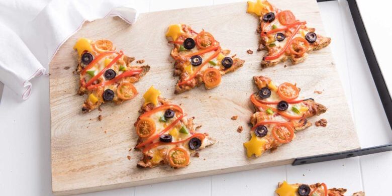 Alt: Seven baked Christmas tree pizzas served on a wooden chopping board.