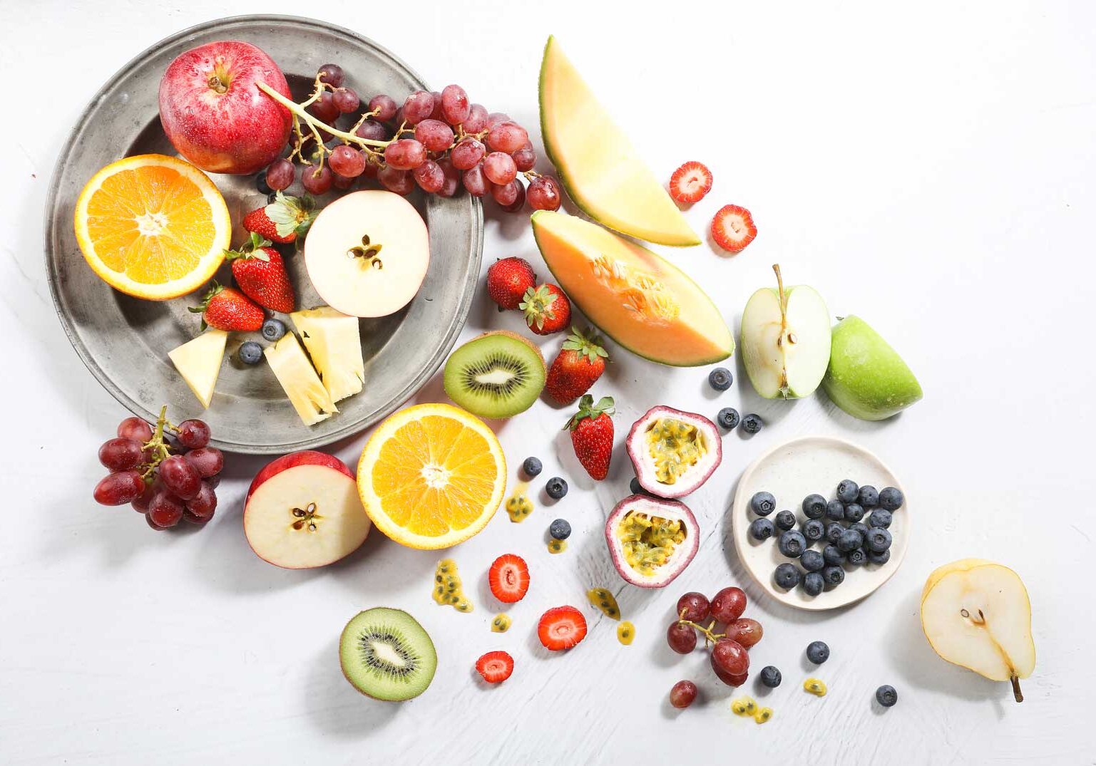A spread of halved fresh fruit scattered across a silver dish and white table