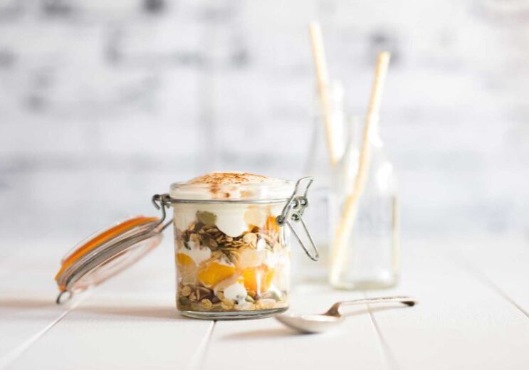 Fruit salad parfait layered in a glass jar with an open lid and a serving spoon on the side.