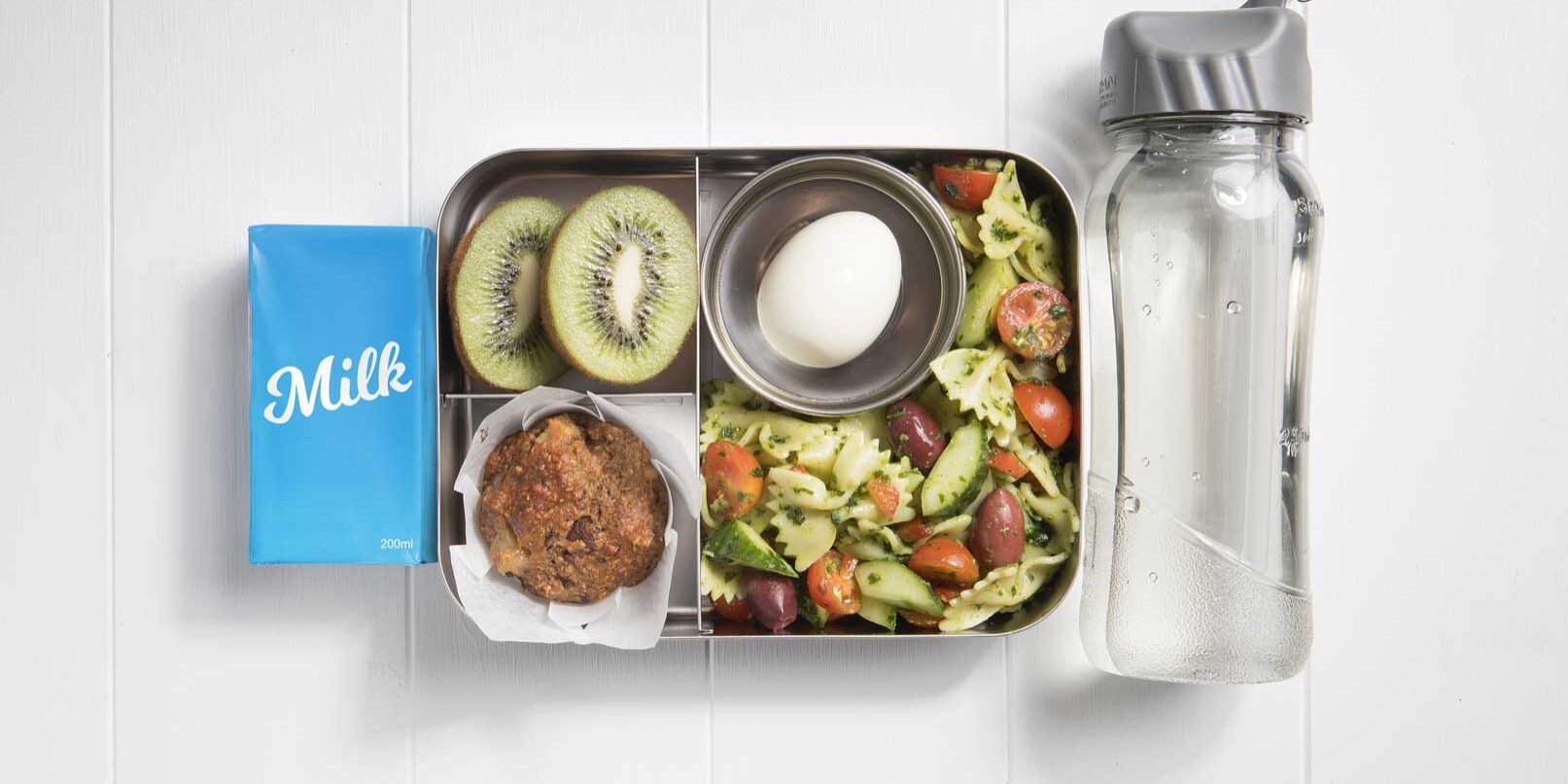 Top view of packed lunch box with salad, muffin, egg, kiwifruit, milk popper and a water bottle.