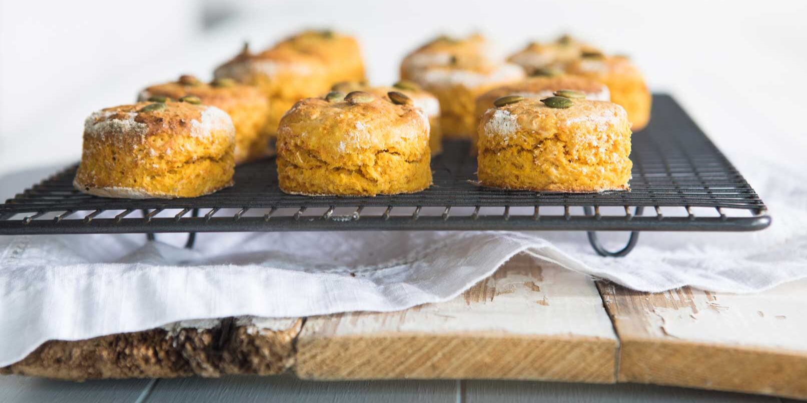 Image of pumpkin and Sweet Potato Scones topped with pepitas and sitting on a cooling rack on a white napkin and wooden chopping board