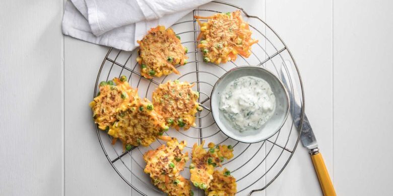 Vegetable fritters on a round wire cooling rack with tzatziki and a knife for spreading to serve.